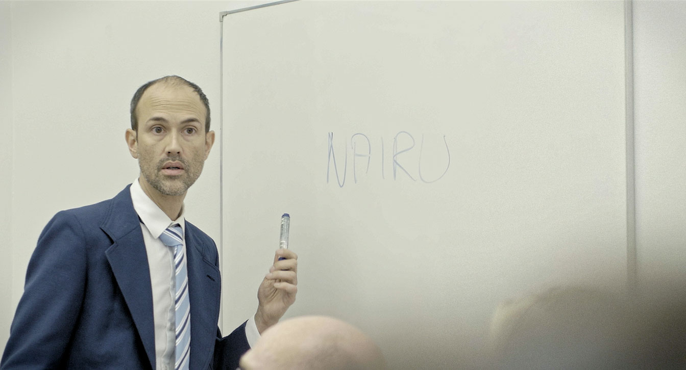 What’s Important Now Is To Feel Bad, film still, Eric Rusch as Job Centre manager in front of a whiteboard.